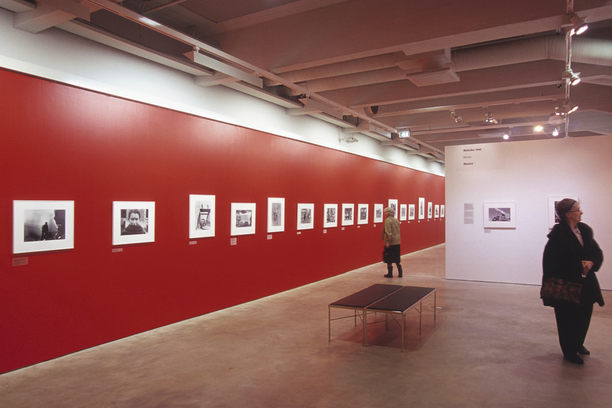 Exhibition space featuring a red wall and black and white photos, illuminated by ERCO lighting.