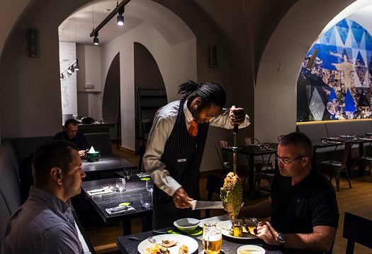 Waiter serving churrasco at Ambiente Brasileiro restaurant, illuminated by ERCO LED lighting.