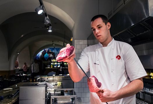 Chef at Ambiente Brasileiro restaurant preparing meat on a skewer, illuminated by ERCO LED spotlights.