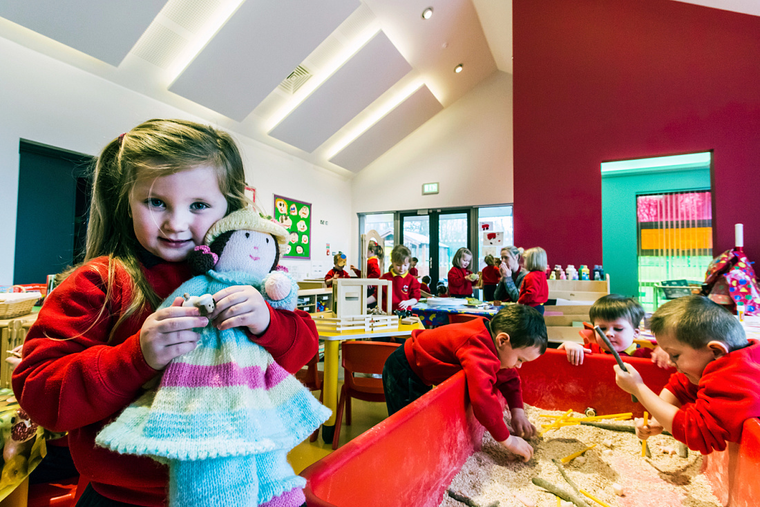 Child with doll at Brontë Nursery, Rathfriland. ERCO LED lighting creates a welcoming atmosphere.