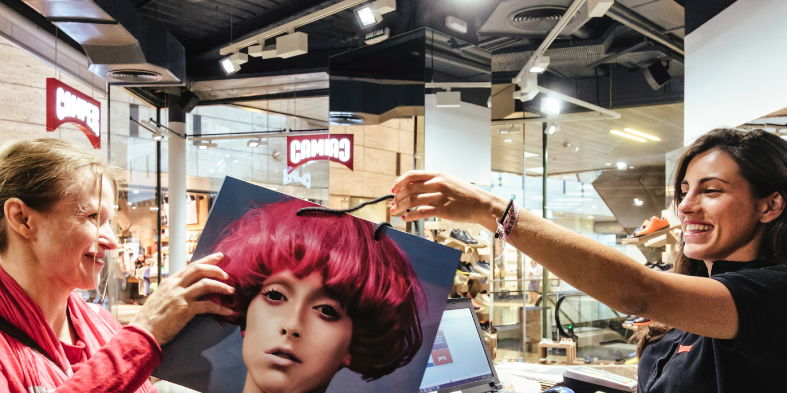 Customer receiving a Camper shopping bag in a shoe store with LED lighting.