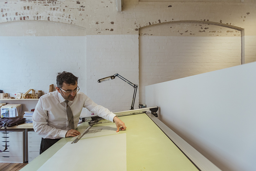 Architect Angelo Candalepas at his drawing board in his Sydney office, lit by ERCO lighting.