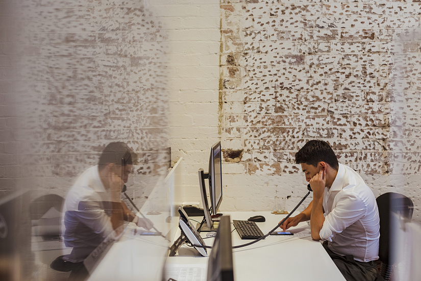 Man on the phone in an office with ERCO lighting, brick wall backdrop.