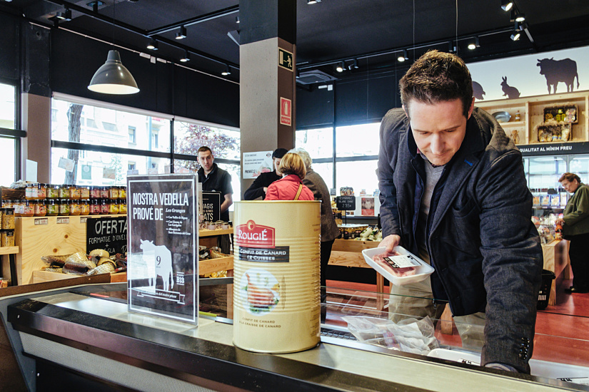 Customer selecting meat products at Casa Tió, illuminated by ERCO LED spotlights for optimal color rendering.