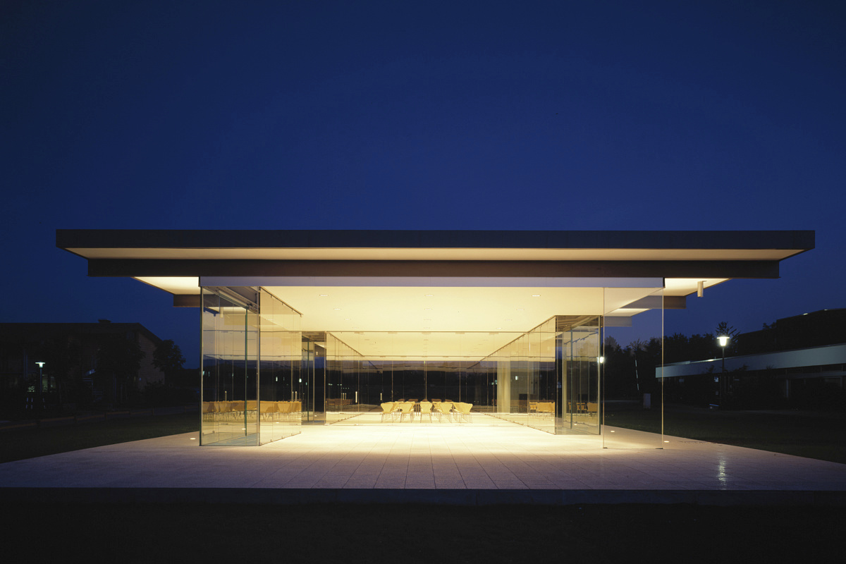 ERCO lighting design: Glass pavilion illuminated with warm white light at dusk.