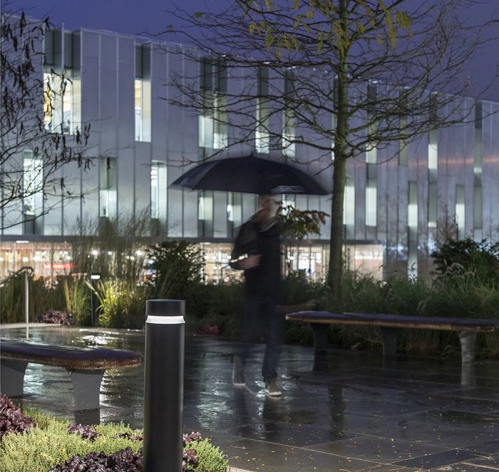 ERCO bollard lighting illuminates a rainy park path for pedestrians at night.