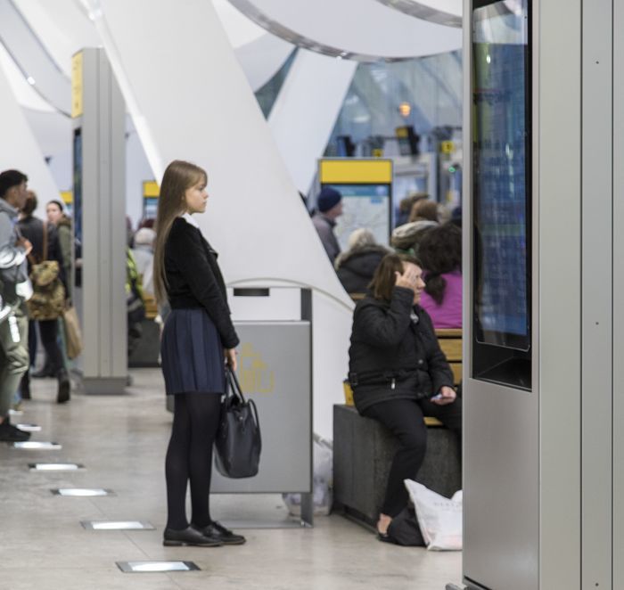 Passengers wait at a train station with ERCO lighting, providing orientation and safety.