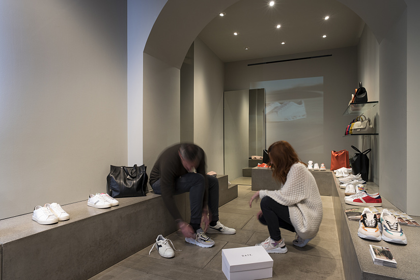 Customers try on D.A.T.E. sneakers in Milan flagship store, lit by ERCO spotlights.