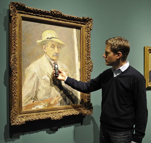 A man measures the damage factor of a painting with a light meter in a museum.