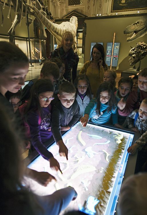 Children explore dinosaur skeletons with an interactive LED table at Viennas Natural History Museum.
