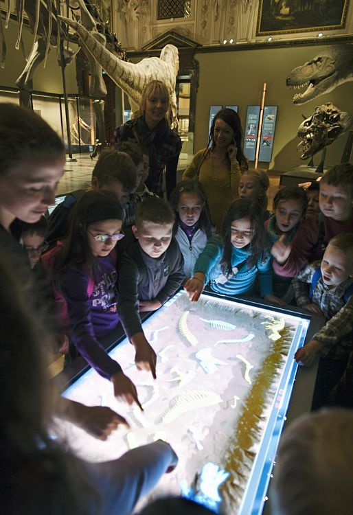 Children explore dinosaur skeletons with an interactive LED table at Viennas Natural History Museum.