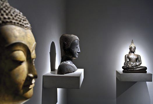 Buddha statues highlighted with directional light in a museum exhibit.