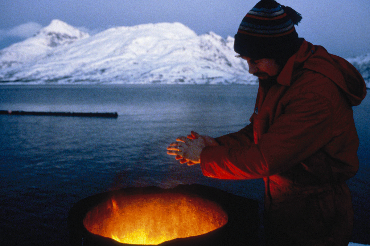 Man warming hands by fire, snowy mountains backdrop, a lighting design concept.