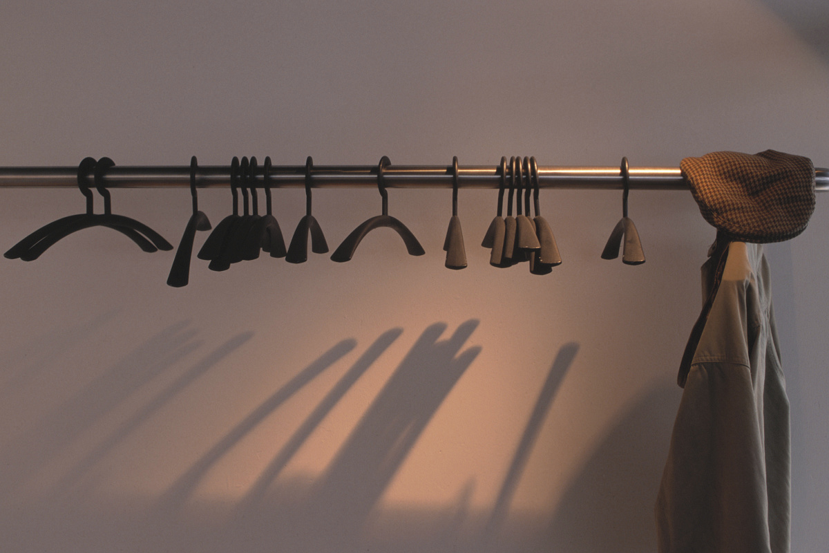 Clothes hangers on a rod with a jacket and hat, casting shadows on the wall.