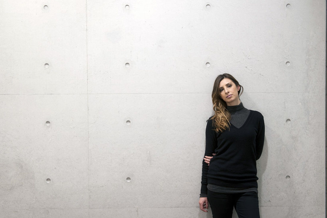 Woman leaning against a concrete wall in the Duvetica showroom, lit by ERCO LEDs.