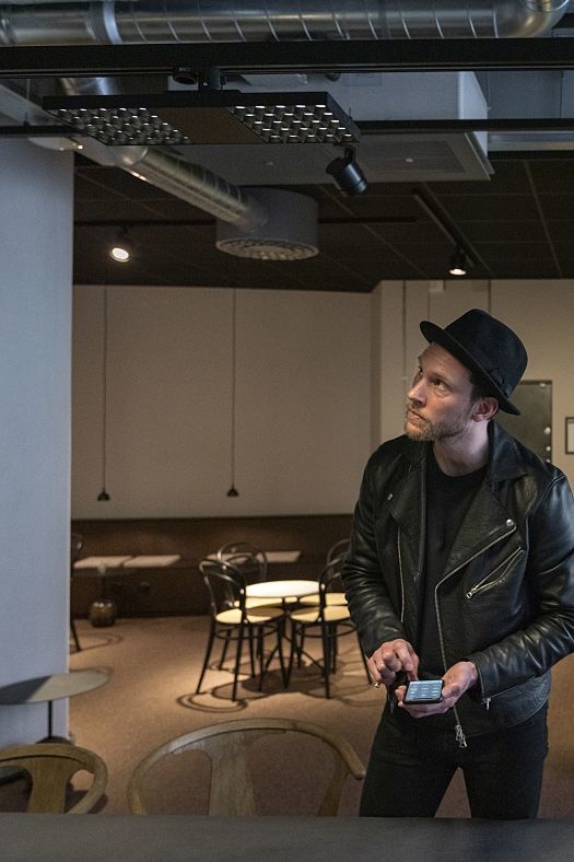 Man with smartphone looking at ERCO Jilly downlights in Fabege co-working space, Stockholm.