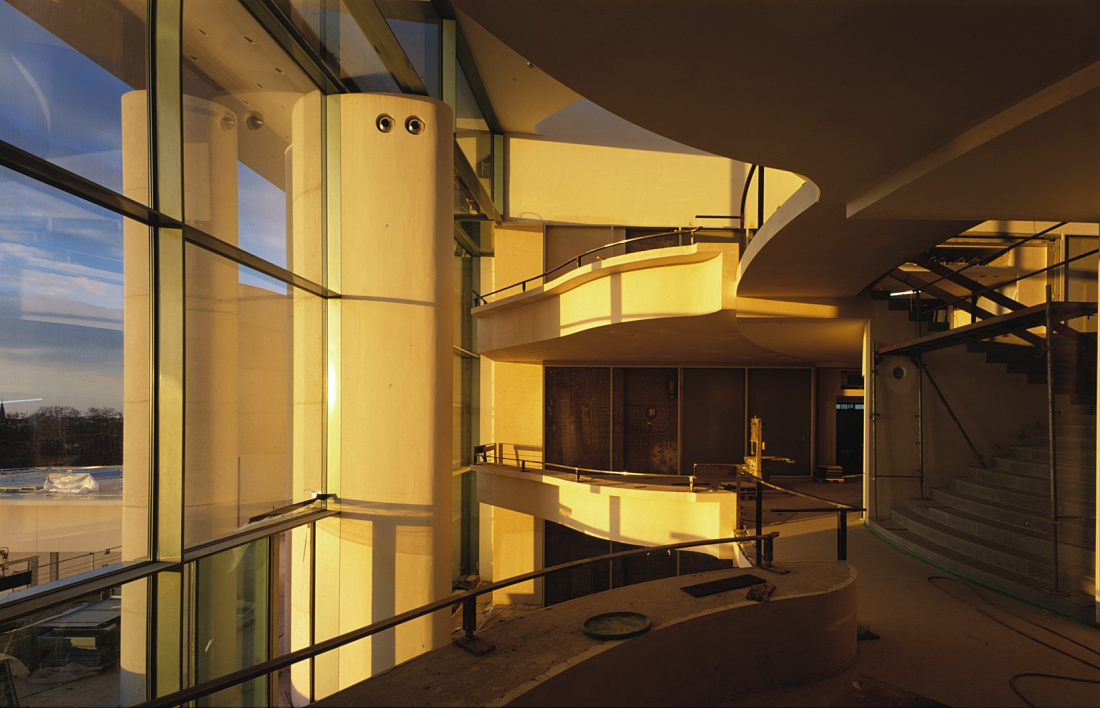 Interior of the Federal Chancellery in Berlin, featuring staircases and window facade in warm light.