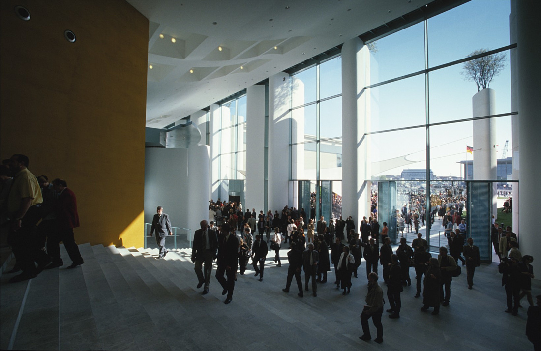 Interior of the Federal Chancellery in Berlin, showing visitors and natural light through large windows.