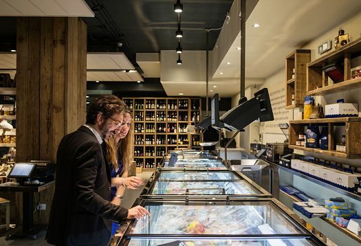 Customers browse gourmet food at Fiorital, illuminated by ERCO LED lighting.