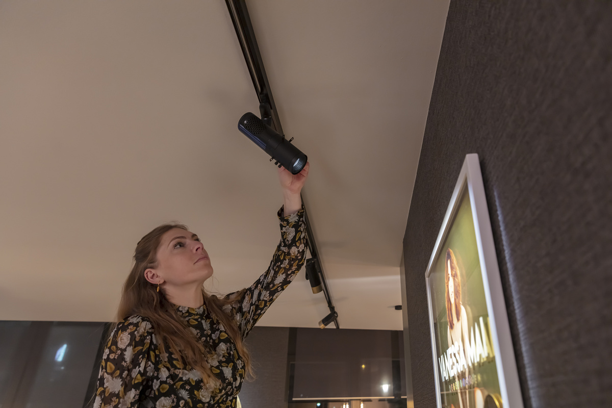 Woman adjusts an ERCO contour spotlight for picture lighting in a gallery.