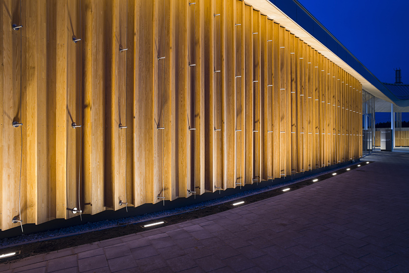 Illuminated wood facade of Fürholzen petrol station with ERCO Site ground-recessed luminaires.