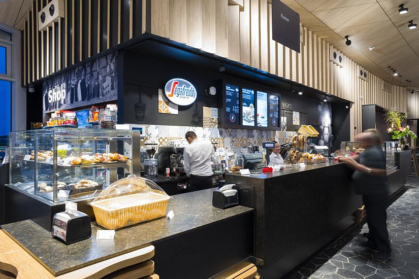 Interior of Segafredo shop at Fürholzen gas station, featuring baked goods and customers.