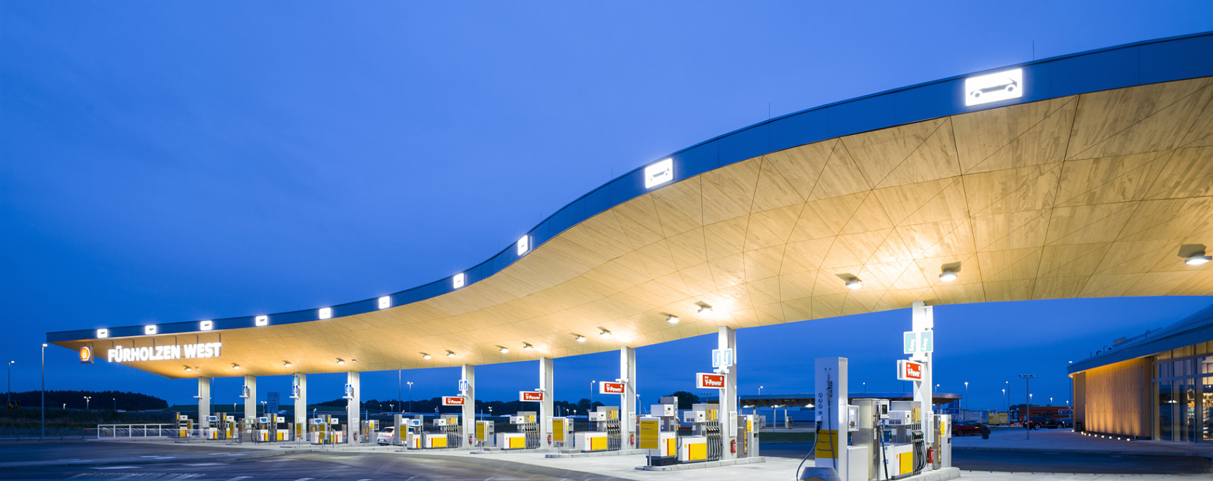 Illuminated Fürholzen gas station with curved roof, designed with ERCO lighting.