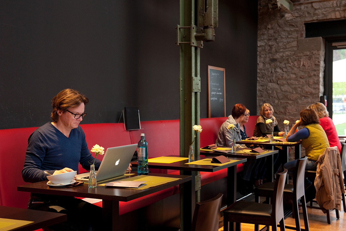 Patron at Halle 32 restaurant in Gummersbach using a laptop. Industrial setting with ERCO lighting.