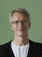 Portrait of a man with glasses against a green background, possibly an architect or lighting designer.