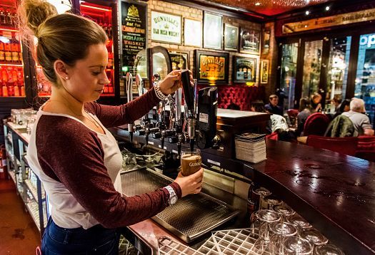 Bartender pouring Guinness at the Harp Bar in Belfast, featuring LED lighting for a traditional pub feel.