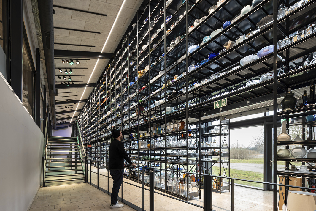 Holmegaard Værk glass museum: Glass art displayed on shelves, illuminated by ERCO LED spotlights.