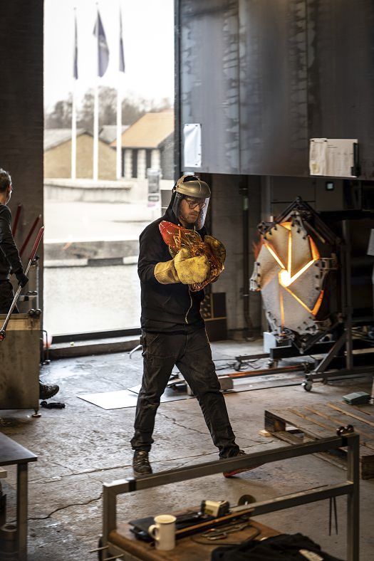 Glassblower shaping glass at Holmegaard Værk, illuminated by ERCO LED spotlights.
