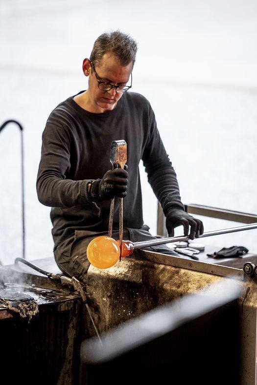 Glassblower shaping a glowing glass orb at Holmegaard Værk museum, Denmark.