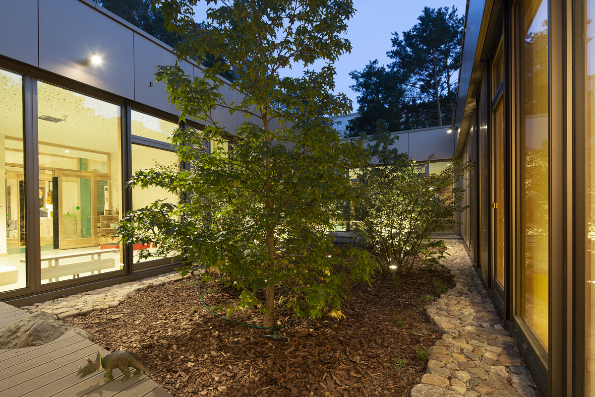 Illuminated outdoor area of Rappelkiste Day Care Center with trees and ERCO lighting for visual comfort.