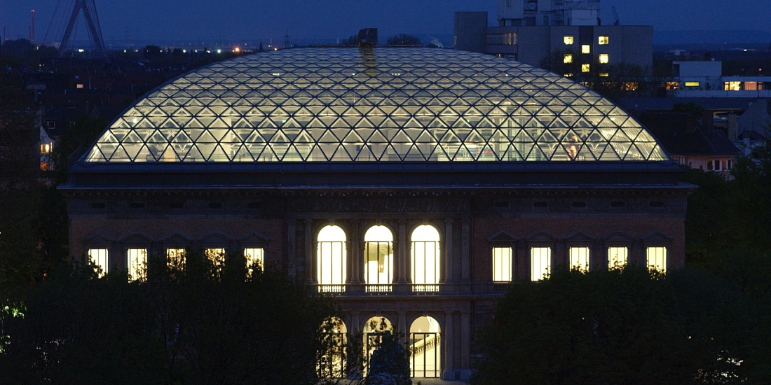 K21 Art Gallery in Dusseldorf featuring an illuminated glass dome at night.
