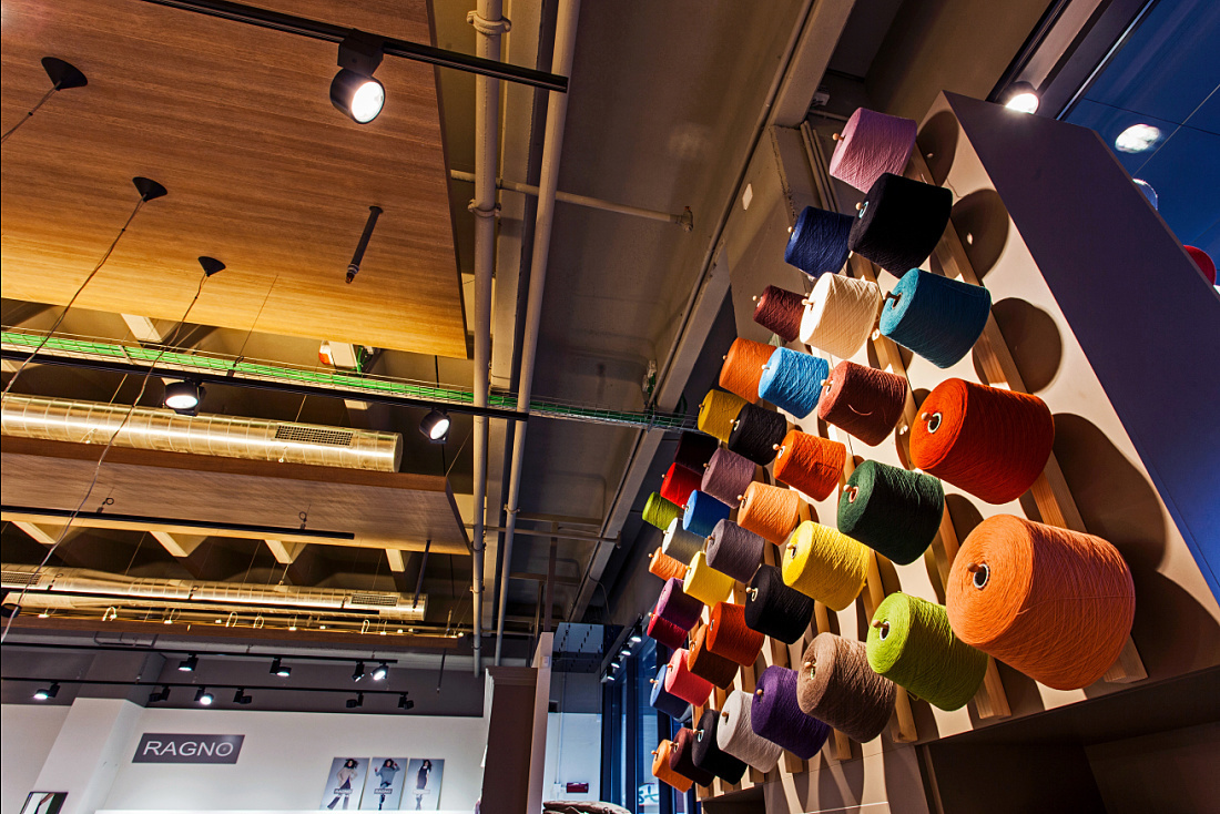Decorative yarn spools wall in Ragno concept store, lit by ERCO Optec spotlights.