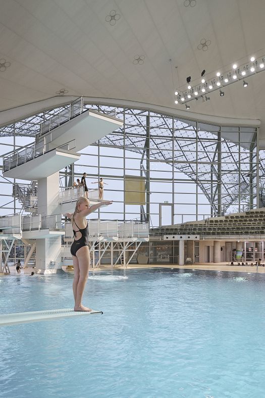 Diver on springboard at Munichs Aquatic Center, lit by ERCO LEDs for energy efficiency and visual comfort.