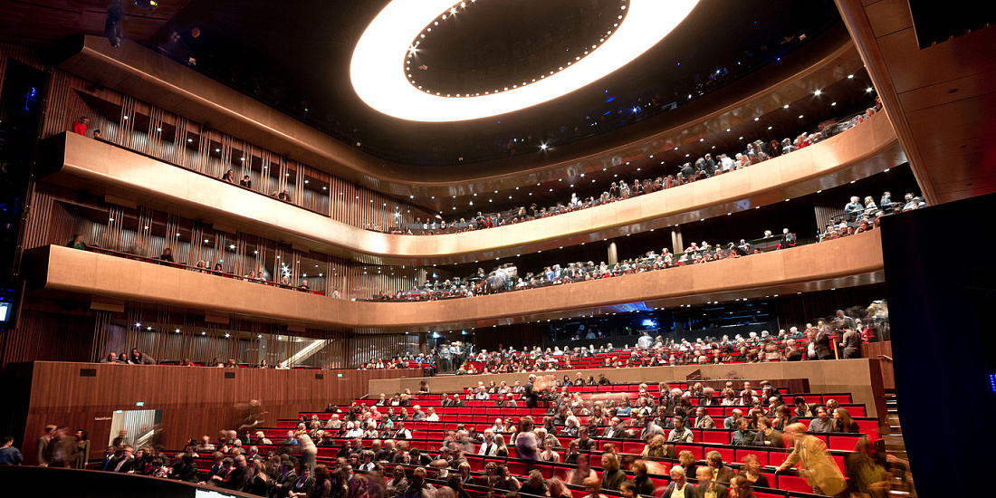 Interior of Linz Music Theatre illuminated by ERCO lighting with an audience.