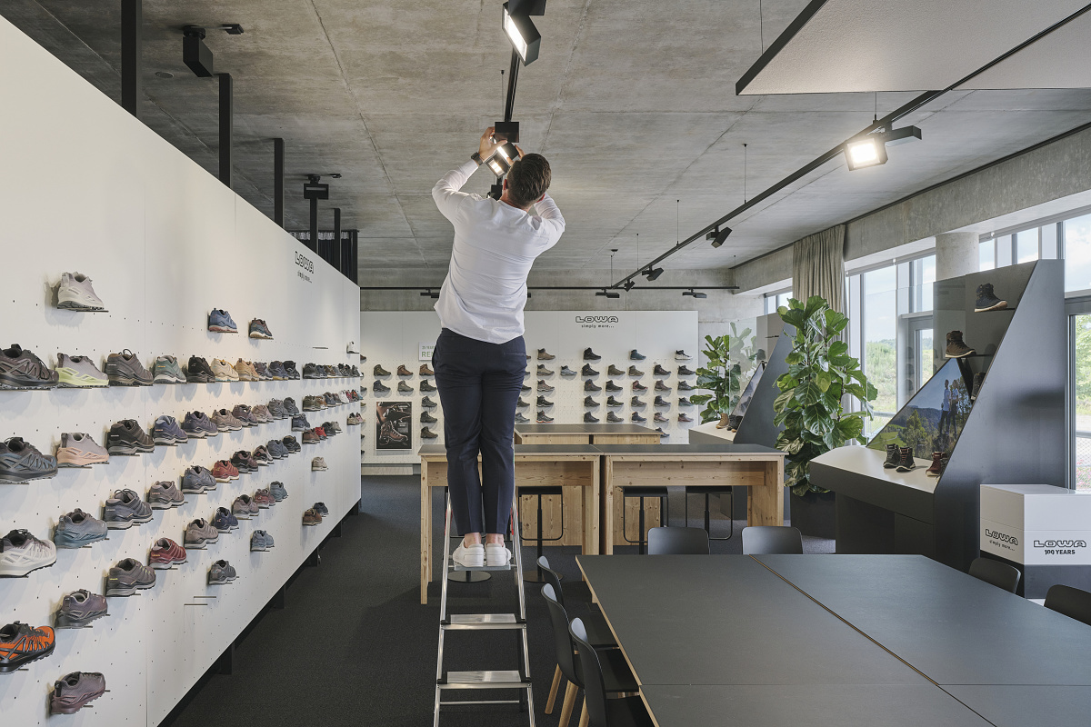 A man adjusts ERCO spotlights in the Lowa office, optimizing lighting for shoe displays.