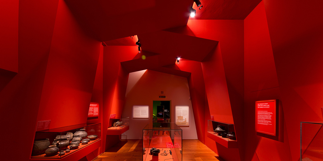 Red exhibition room in MAMUZ Museum Mistelbach featuring archaeological finds, lit by ERCO spotlights.