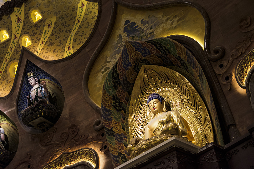 Golden Buddha statue in Usnisa Palace, Nanjing, illuminated by ERCO LED spotlights for spiritual contemplation.