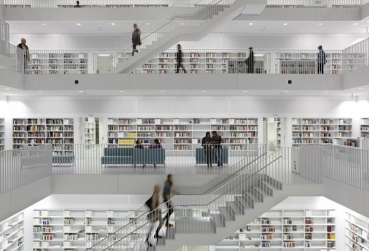 Interior of a multi-story library with stairs and shelves full of books, illuminated with ERCO lighting.