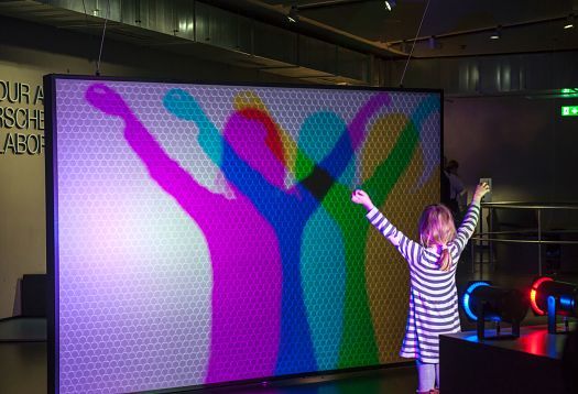 Child interacting with colored shadows on a light wall at the Phänomenta Science Center, Lüdenscheid.