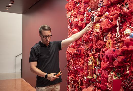 A man uses a photometer to measure illuminance on a red art installation.