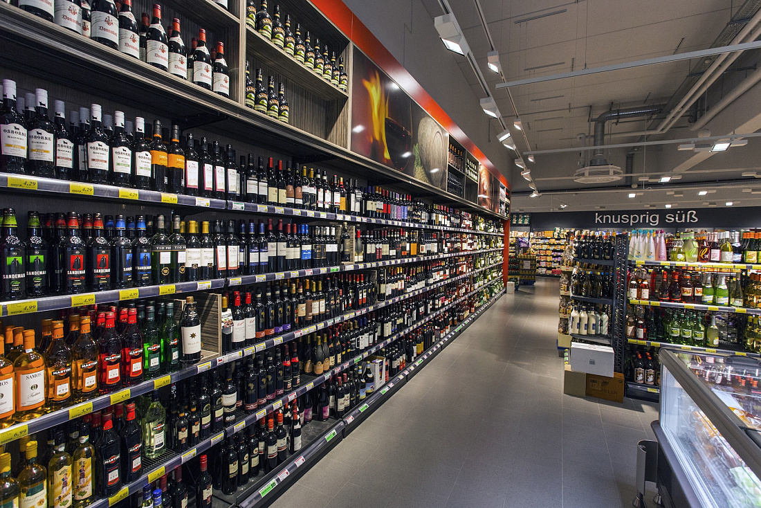 Wine and spirits aisle in REWE supermarket, illuminated by ERCO Opton LED spotlights for accent lighting.