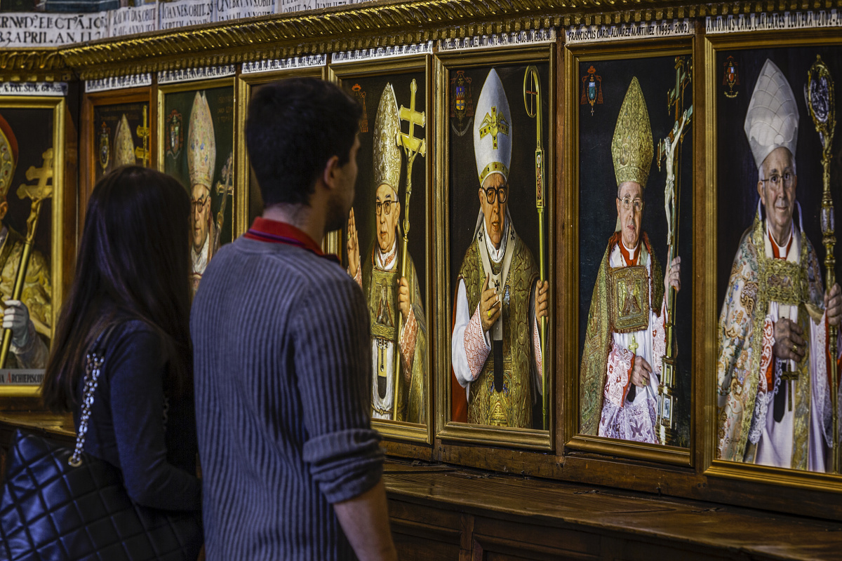 Visitors view illuminated portraits of Archbishops in the Sala Capitular, Toledo Cathedral.