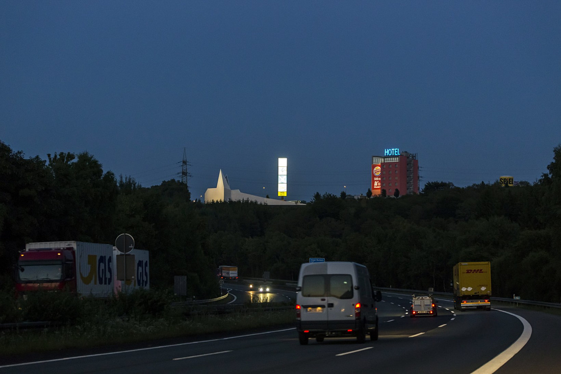 Siegerland Motorway Church at night, illuminated, next to a hotel and fast food restaurant.