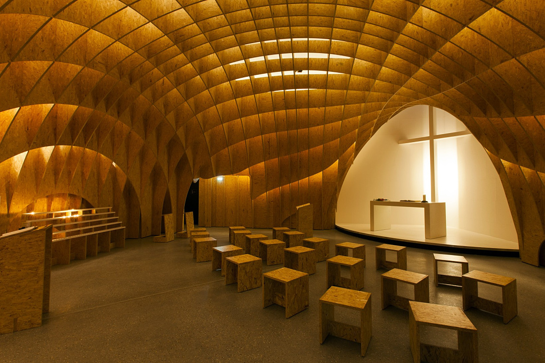 Siegerland Motorway Church interior featuring wooden structure and cross, illuminated by ERCO lighting.