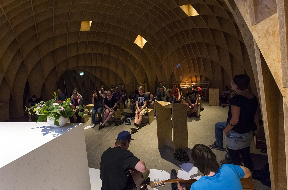 Interior of Siegerland Motorway Church with visitors and musicians, lit by ERCO lighting.