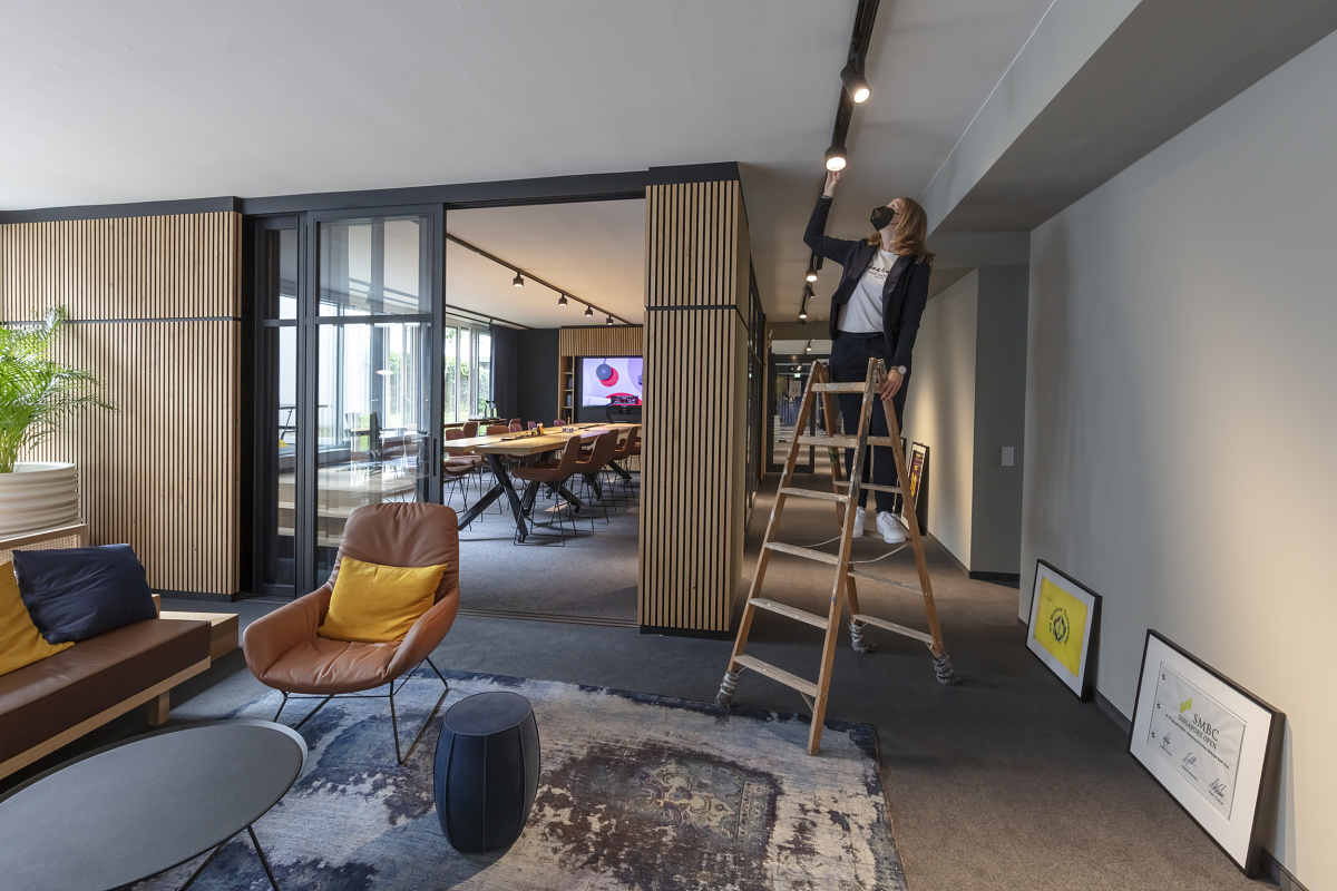 Woman adjusts ERCO Parscan spotlights on a track in the Sportfive office, Hamburg.